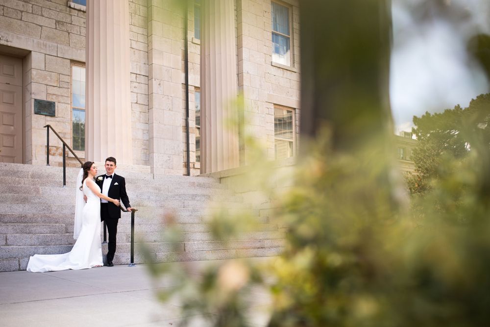 Side view of elegant wedding couple on stone steps with soft focus greenery in foreground.  Iowa City wedding photographer.