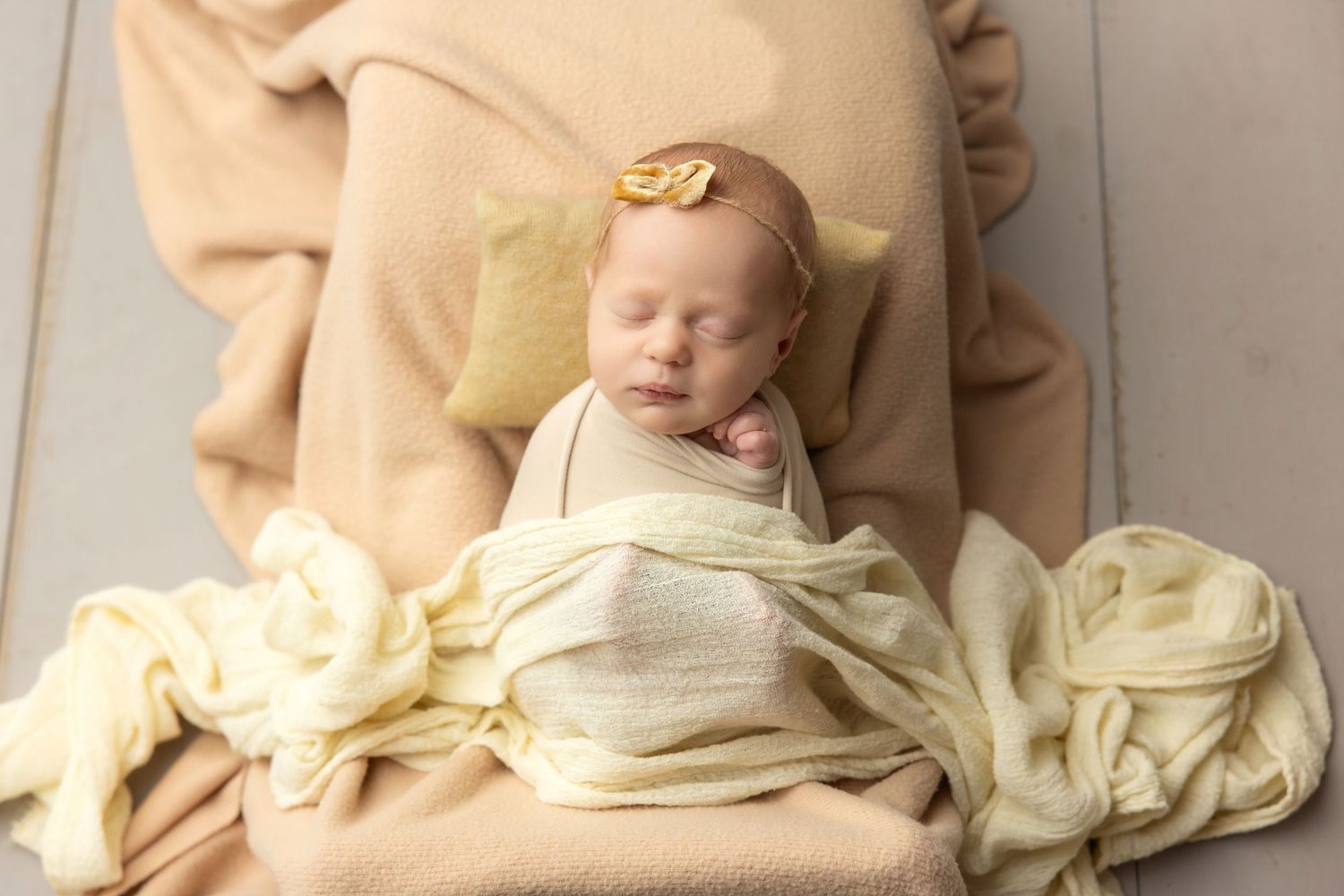 Newborn baby wrapped in teal swaddle holding green knit bear toy, resting in decorative bucket.