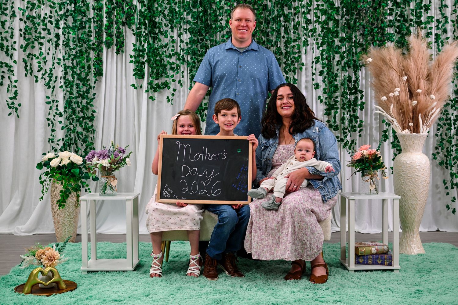 Family of five posing for a Mother's Day 2026 photo with a chalkboard sign in a decorated studio.