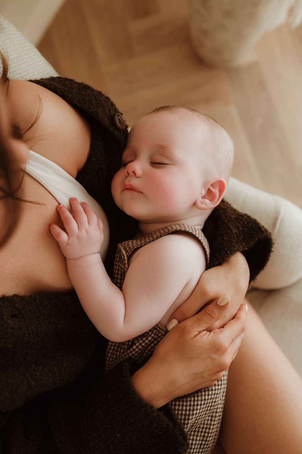 A peacefully sleeping baby in a checkered romper cradled in mothers arms during a warm natural light photoshoot.