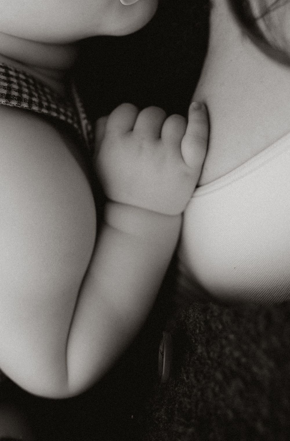 Close-up black and white photo of baby hand resting on mothers chest in checkered outfit.