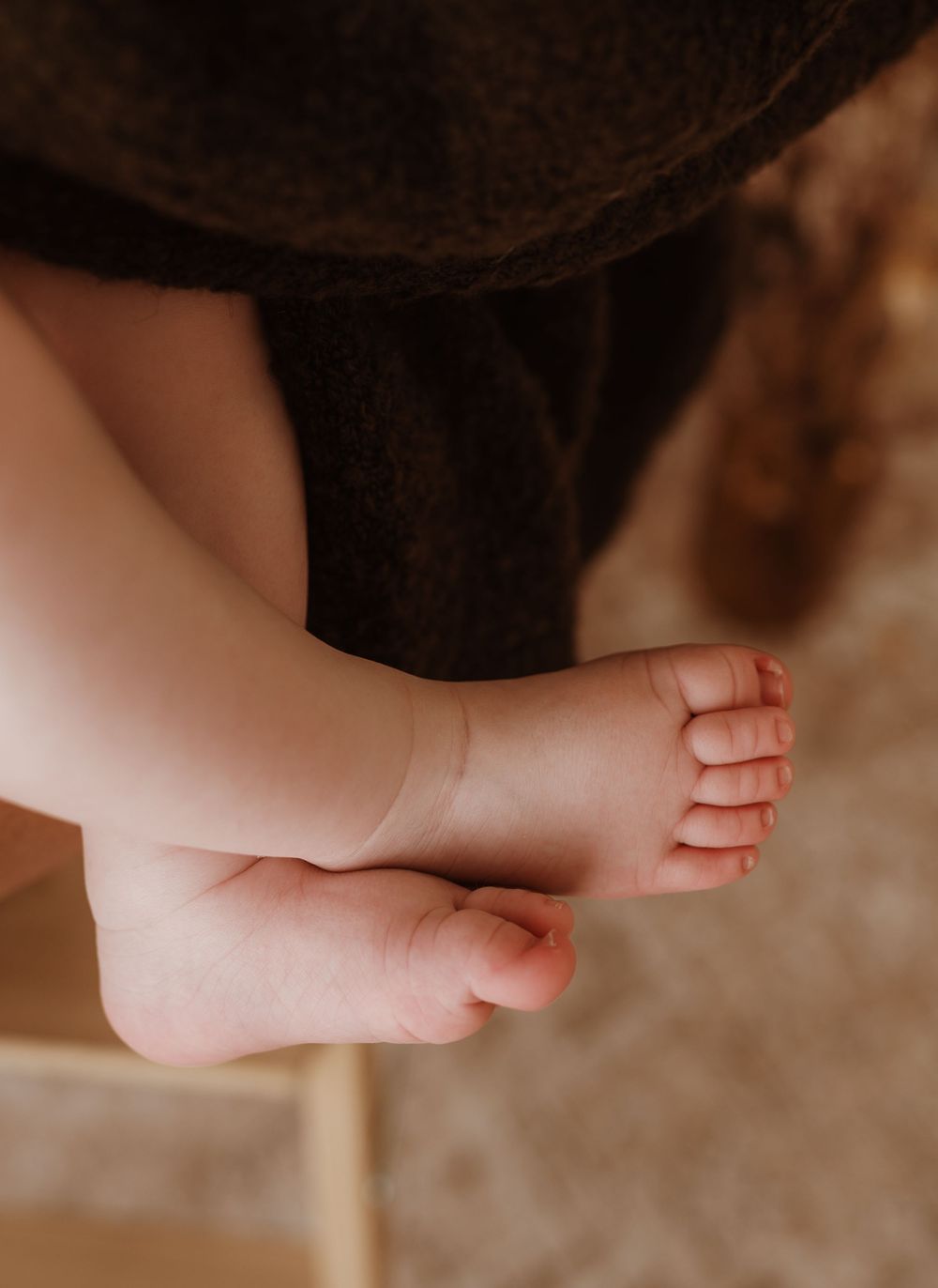 Close-up of tiny newborn baby feet dangling against dark fabric clothing.