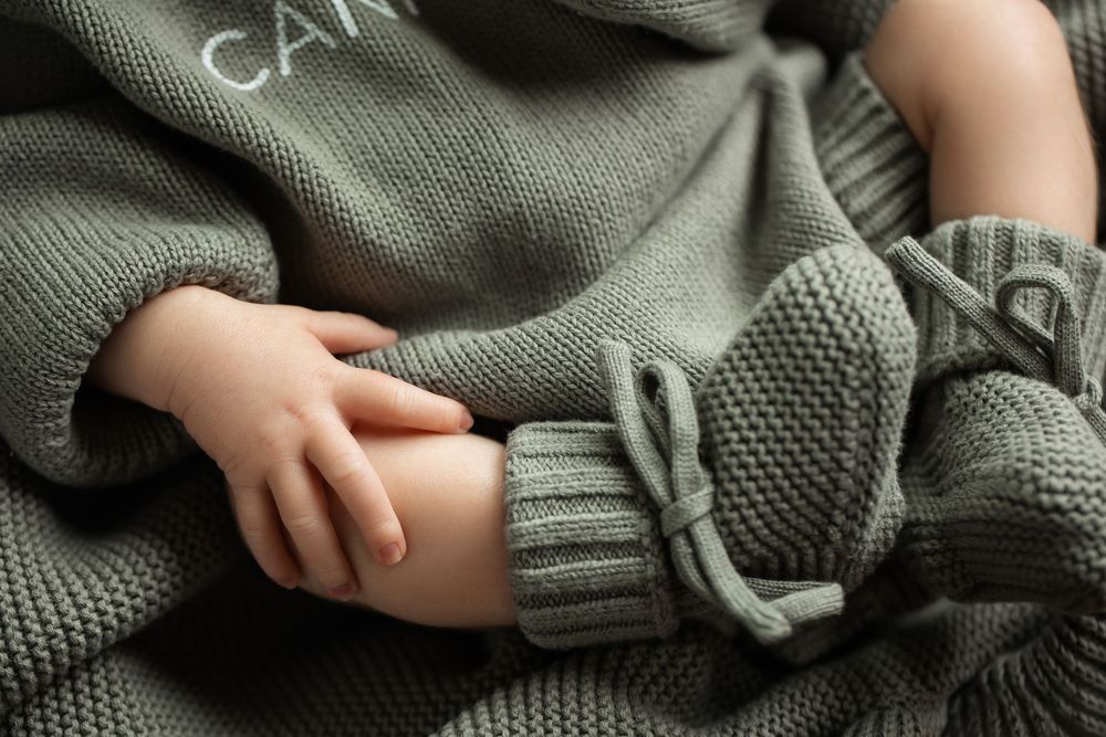 Detail shot of newborn baby hands and feet in sage green knit Cannon outfit.