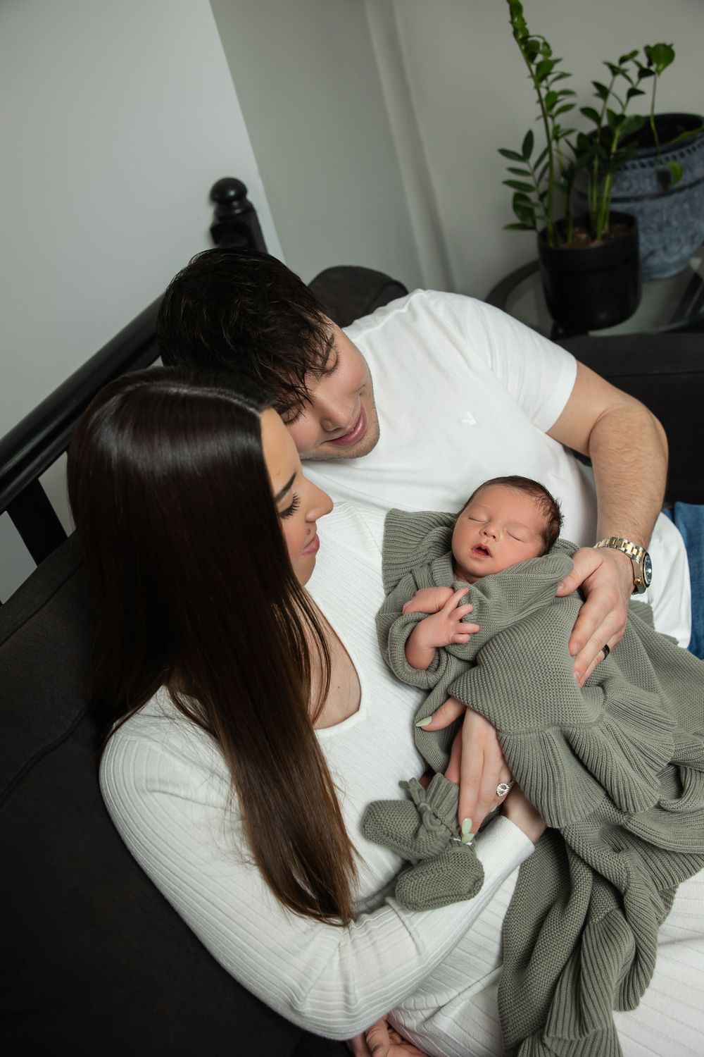 New parents gazing lovingly at their newborn baby wrapped in sage green knit blanket.