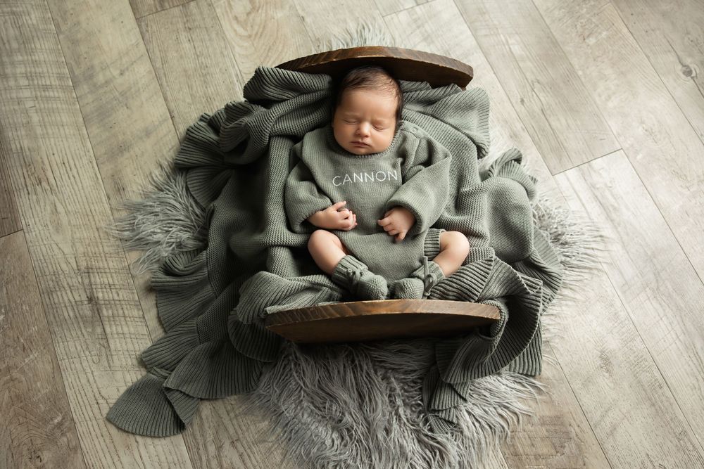 Sleeping newborn baby named Cannon wrapped in sage green blanket in wooden bowl prop.