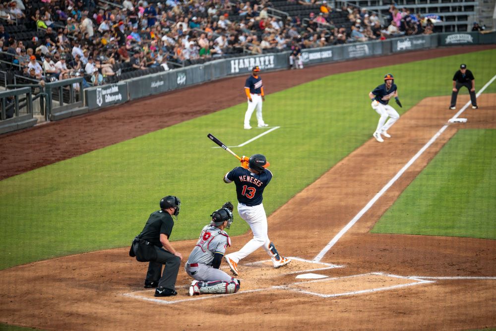 Baseball player number 13 swinging bat at home plate with umpire and catcher during a stadium game.