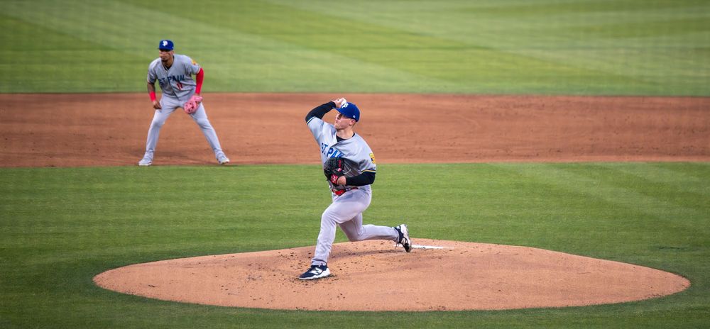 Baseball pitcher in blue uniform delivering a pitch on a professional stadium mound during a game.