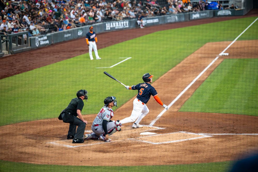 Baseball batter swings at pitch during professional game with umpire and catcher at home plate.