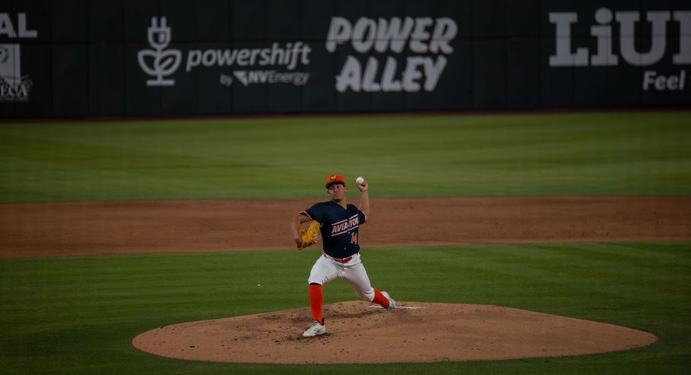 Baseball pitcher delivers pitch at Power Alley stadium under bright lights during night game.