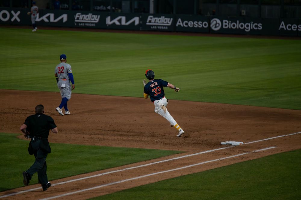 Baseball player rounds third base during game with Kia and Findlay sponsorship signs visible.