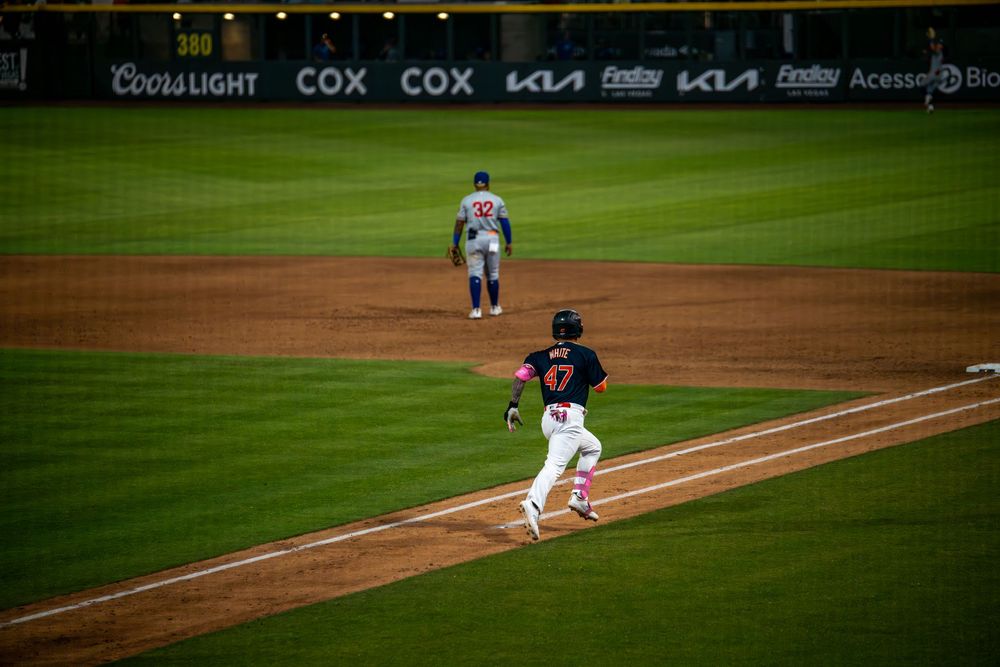 Baseball player rounds third base as opponent watches during professional minor league game.