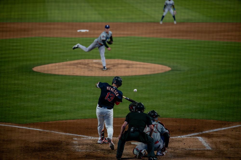 Baseball batter makes contact with pitch as catcher and umpire observe during night game.