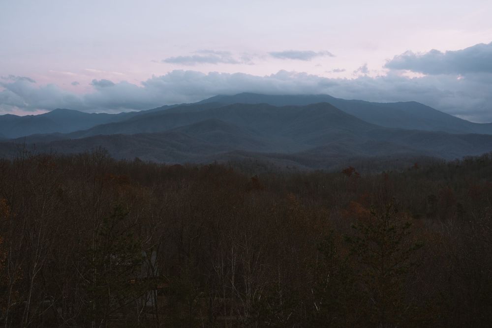 Smoky Mountains panoramic view at dusk with layered blue ridges and colorful autumn forest in foreground.