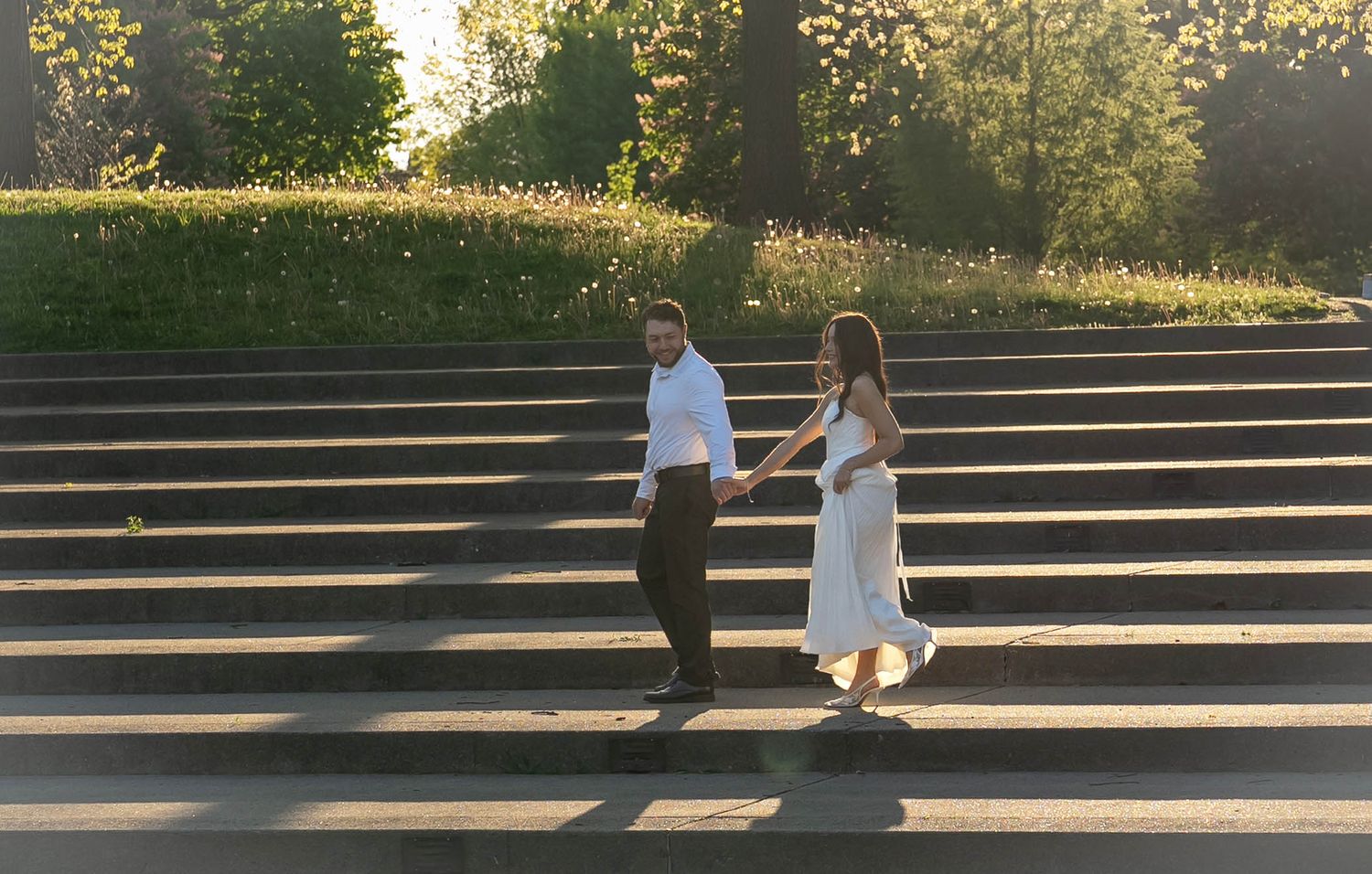 Couple holding hands walking down sunlit outdoor stone steps at Franklin Park for Engagement Photos
