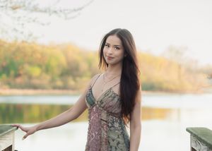 Young woman in a floral sundress posing gracefully on a wooden bridge by a scenic autumn lake.