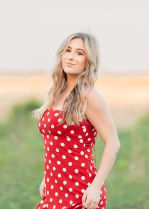 Young woman with blonde wavy hair wearing a red and white polka dot strapless dress outdoors.