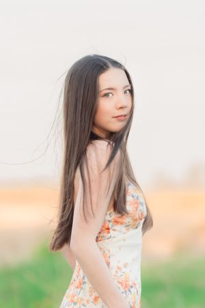 Young woman with long dark hair in floral dress poses outdoors in soft natural light.