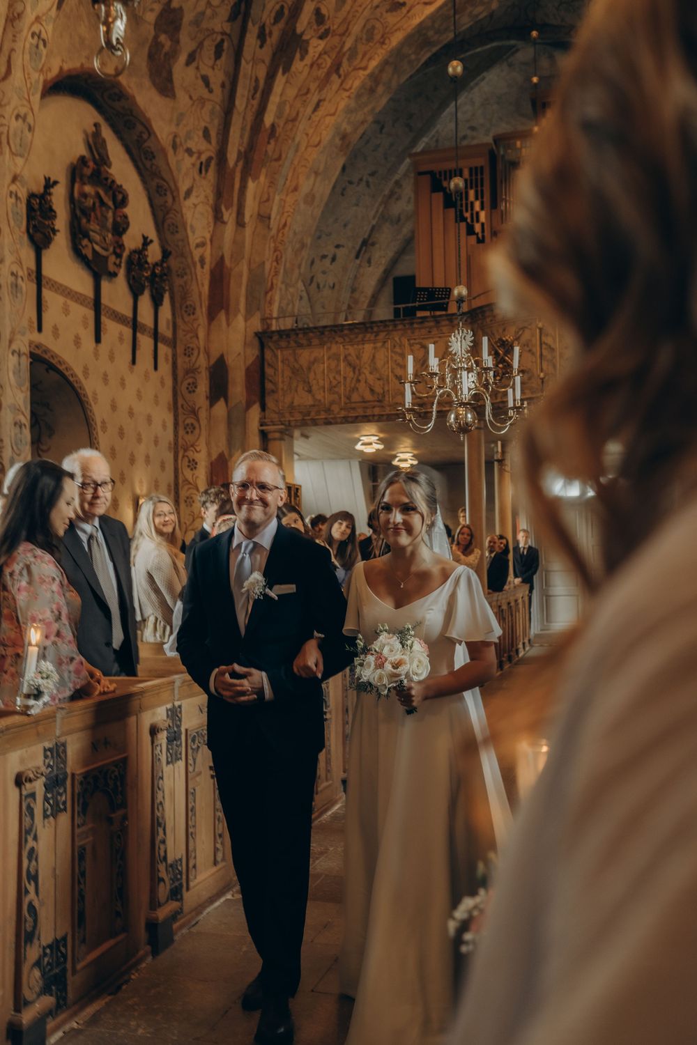 wedding guests looking and bride and father walking into church while being captured by authentic wedding photographer in Stockholm