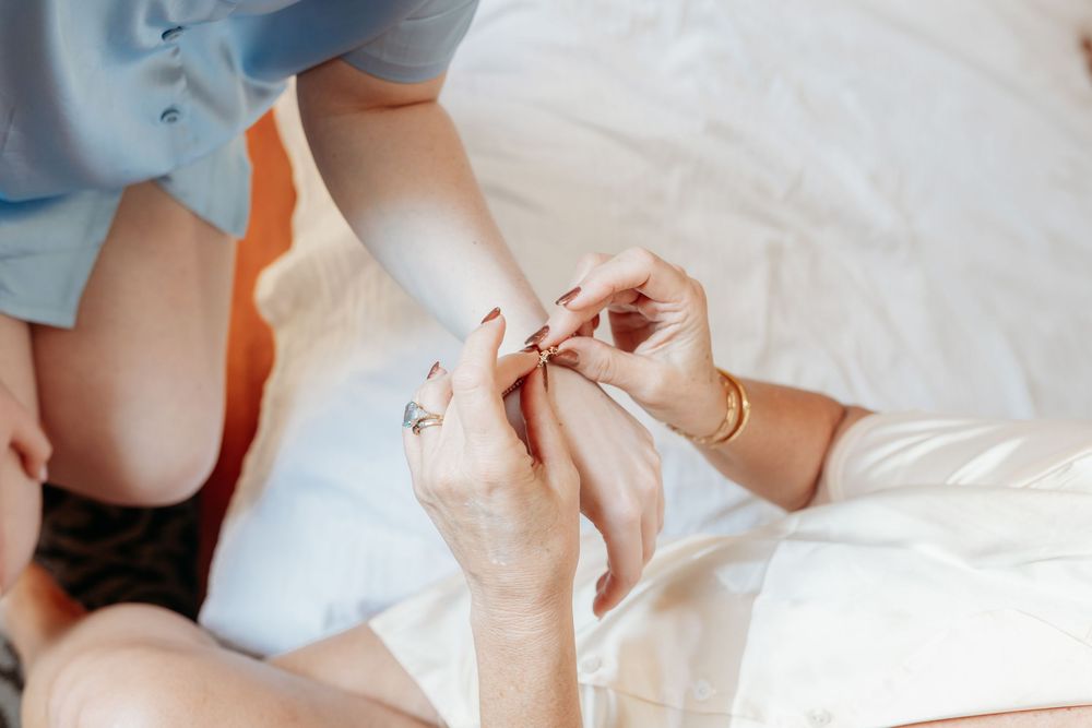 A person fastening a delicate bracelet onto a bride's wrist during wedding preparations.