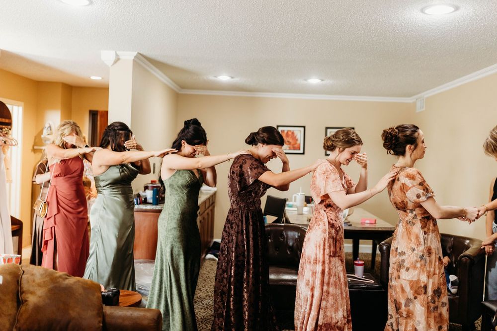 Bridesmaids in colorful mismatched dresses holding hands in a line during wedding preparations.