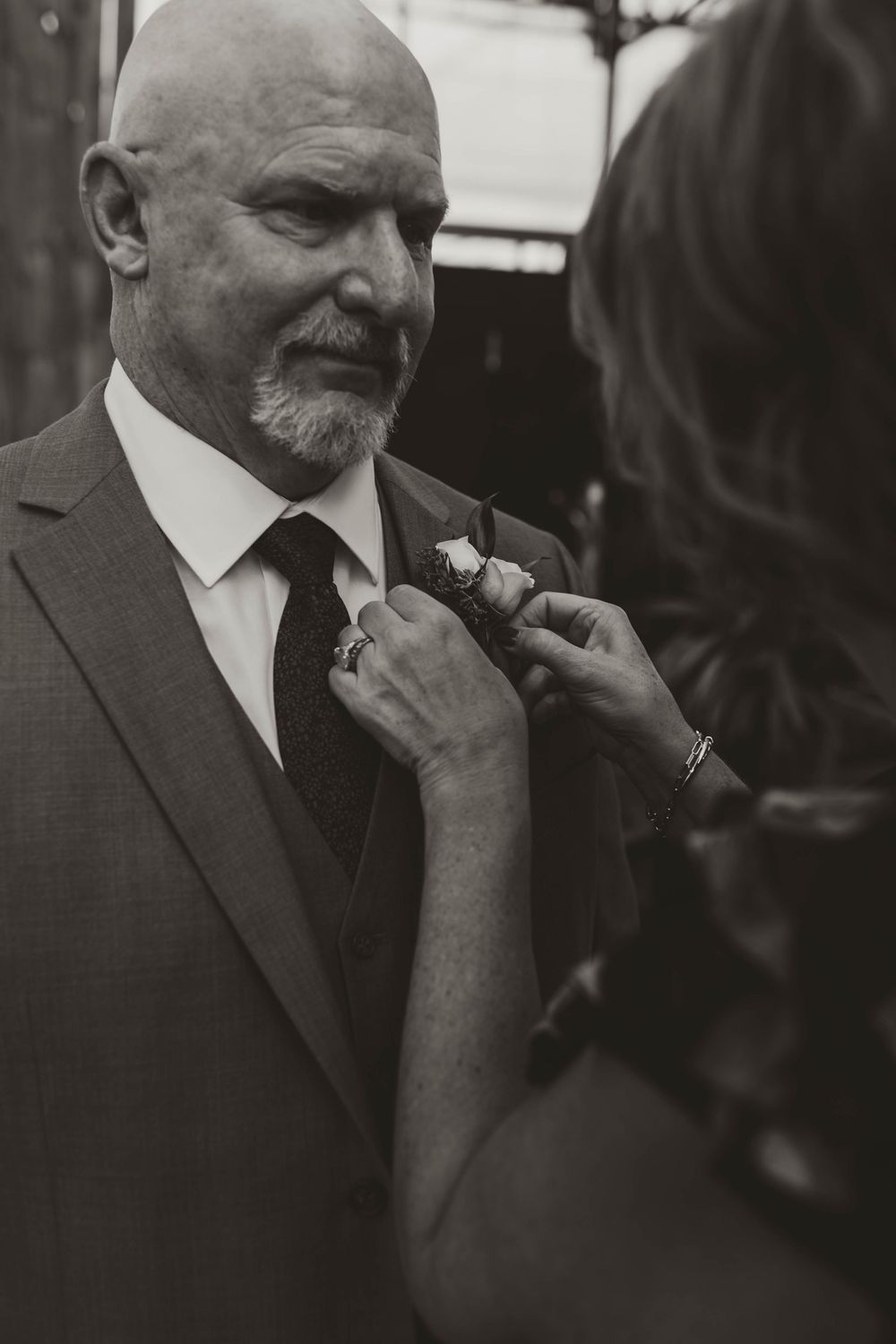 Black and white photo of a bald man in a suit having a boutonniere pinned to his lapel.