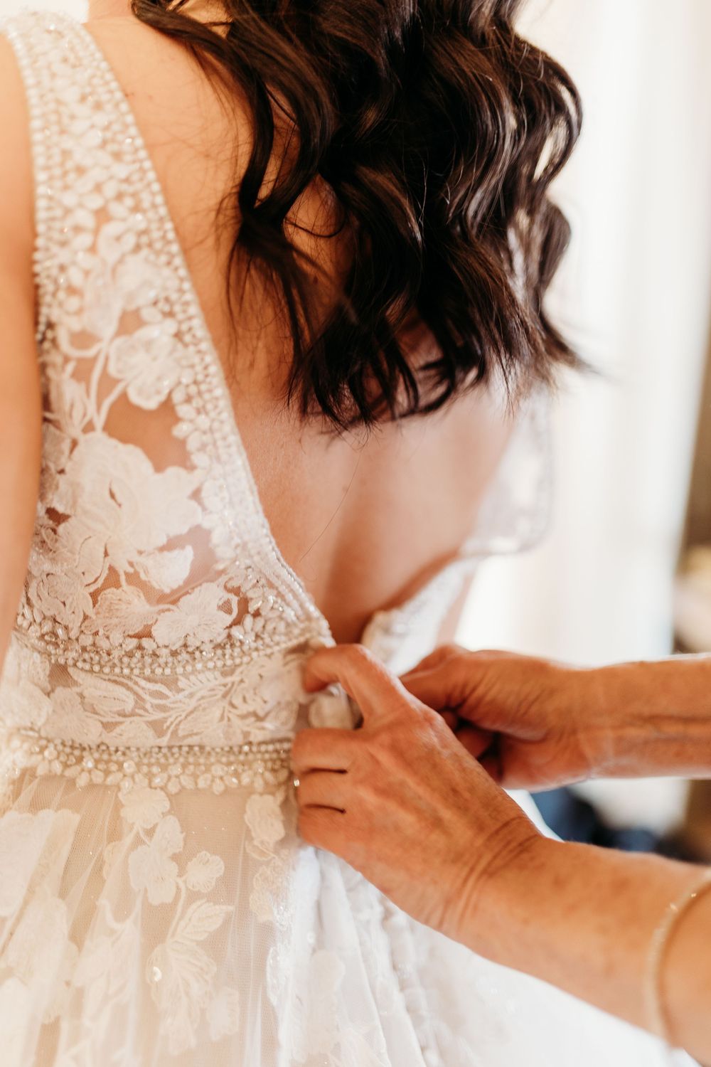 Close-up of hands fastening the back of a bride's intricate lace wedding gown.