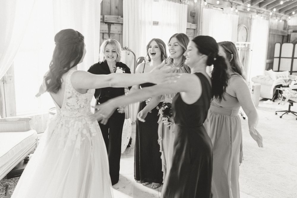 Black and white photo of bridesmaids reaching out to embrace bride during wedding preparations.