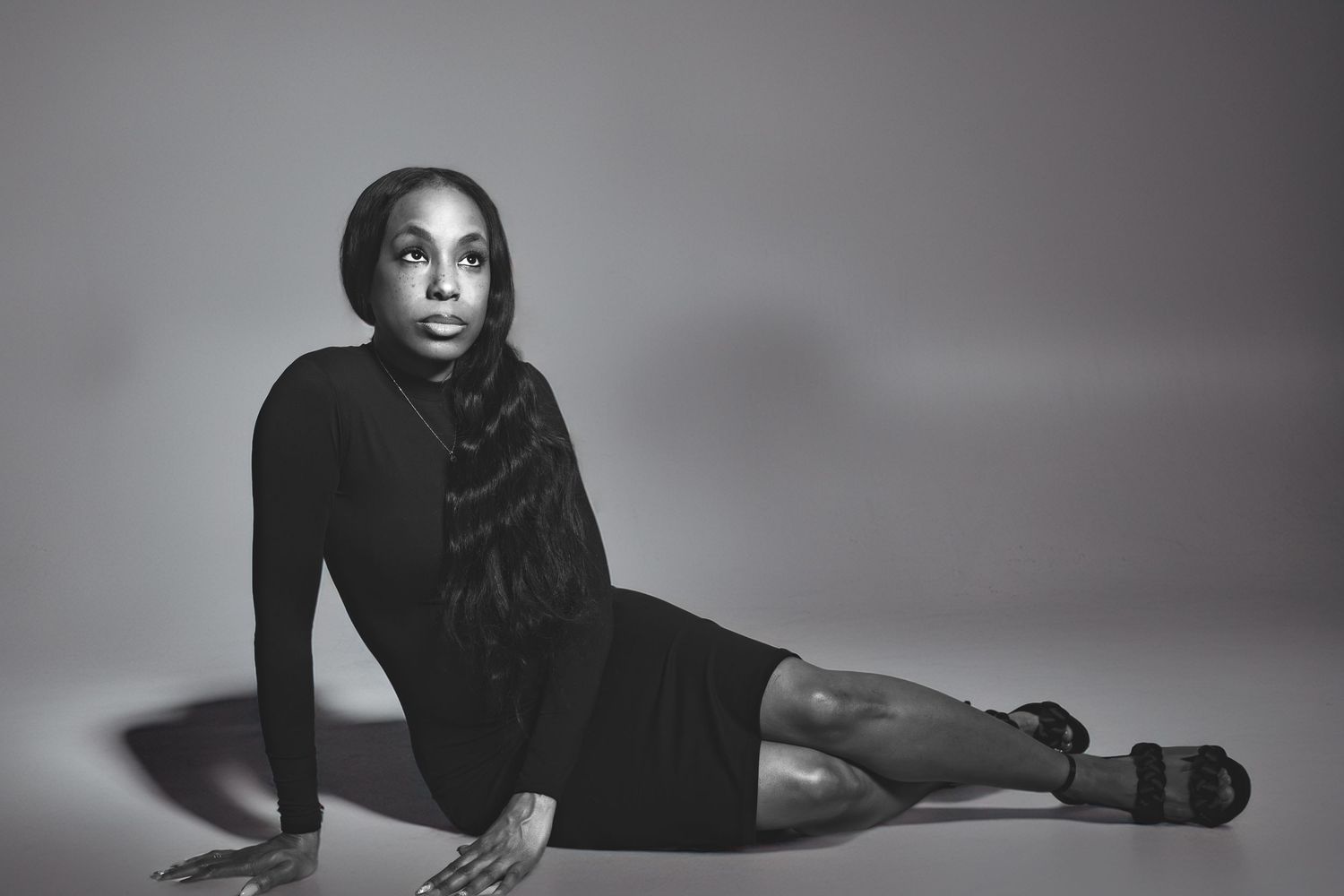 Black and white photo of a woman in a black dress posing gracefully on the floor against a neutral background.