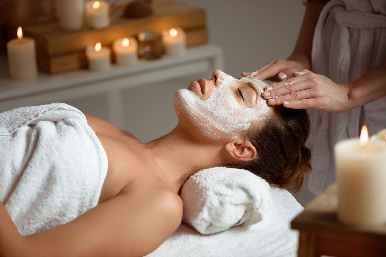 Woman receiving a relaxing facial mask treatment at a luxury spa with candles in the background.