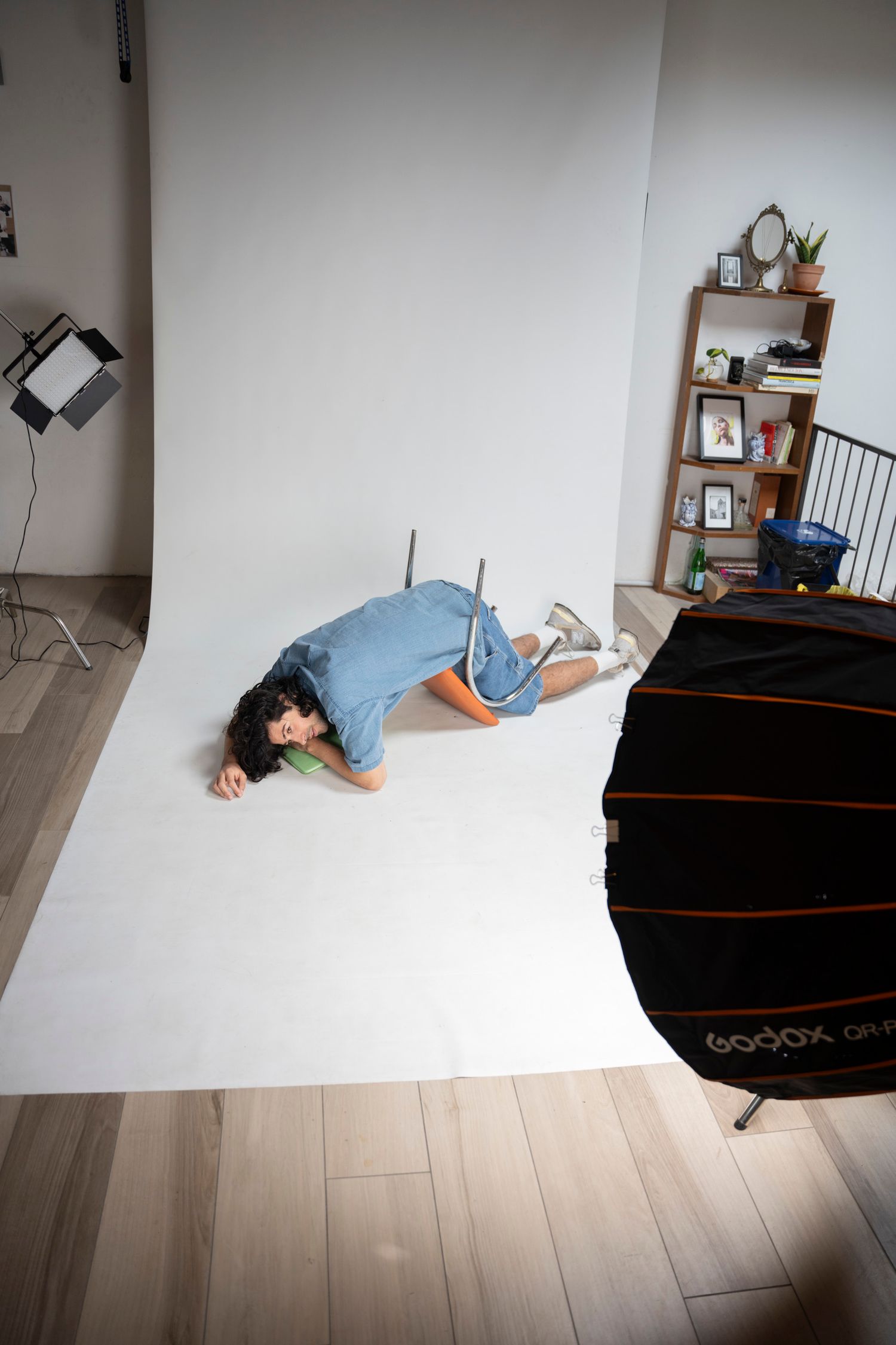 Person in blue outfit lying on white backdrop in a photography studio with softbox lighting equipment.