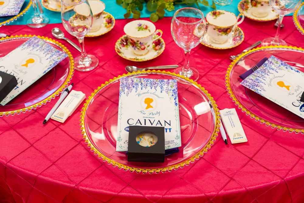 Elegant pink table setting with gold-rimmed charger plates, floral teacups, and a Caivan book as decor.