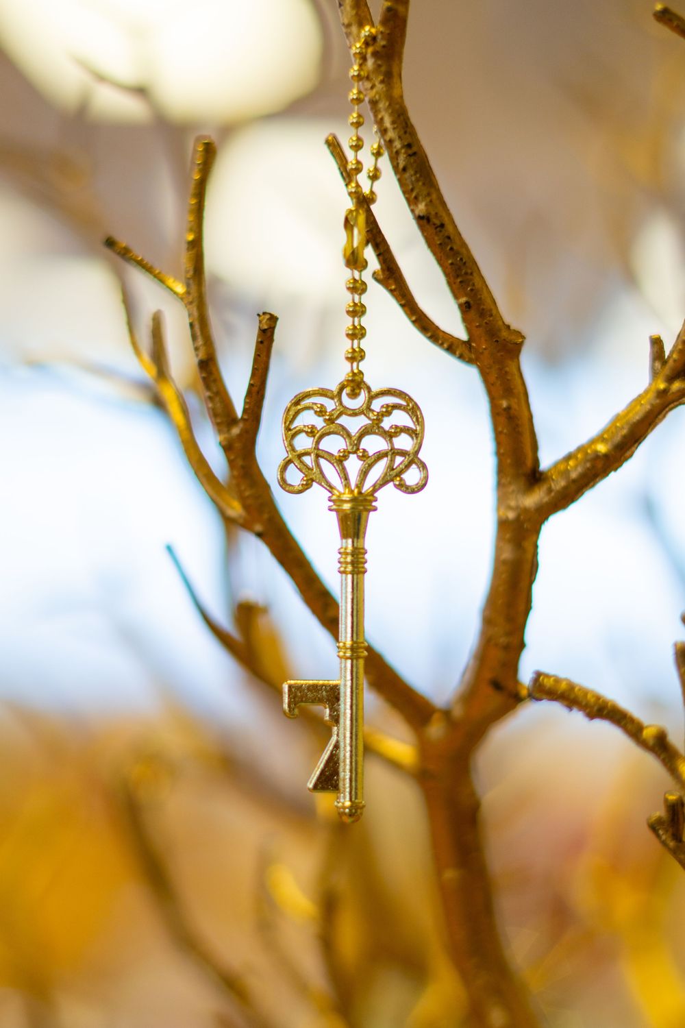 Golden ornate skeleton key hanging from a decorative gold branch, with a blurred bokeh background.