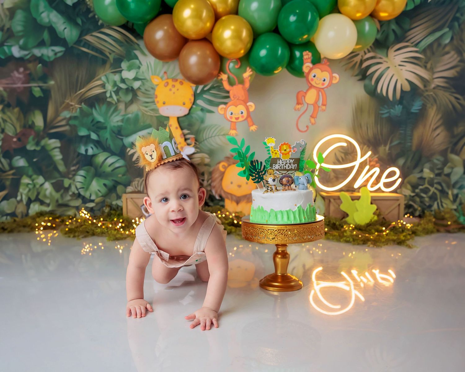 Baby's first birthday jungle safari cake smash with green balloons, animal decorations, and glowing One neon sign.