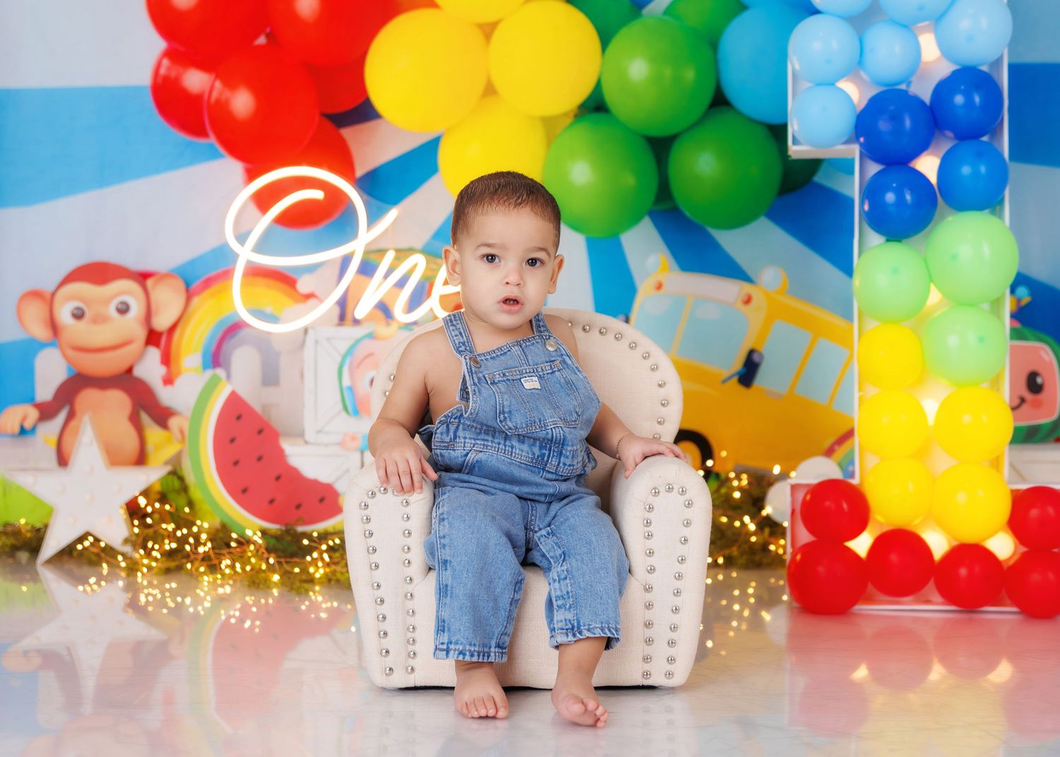 Baby's first birthday cake smash with rainbow balloons, colorful decorations, and a white gold throne chair.