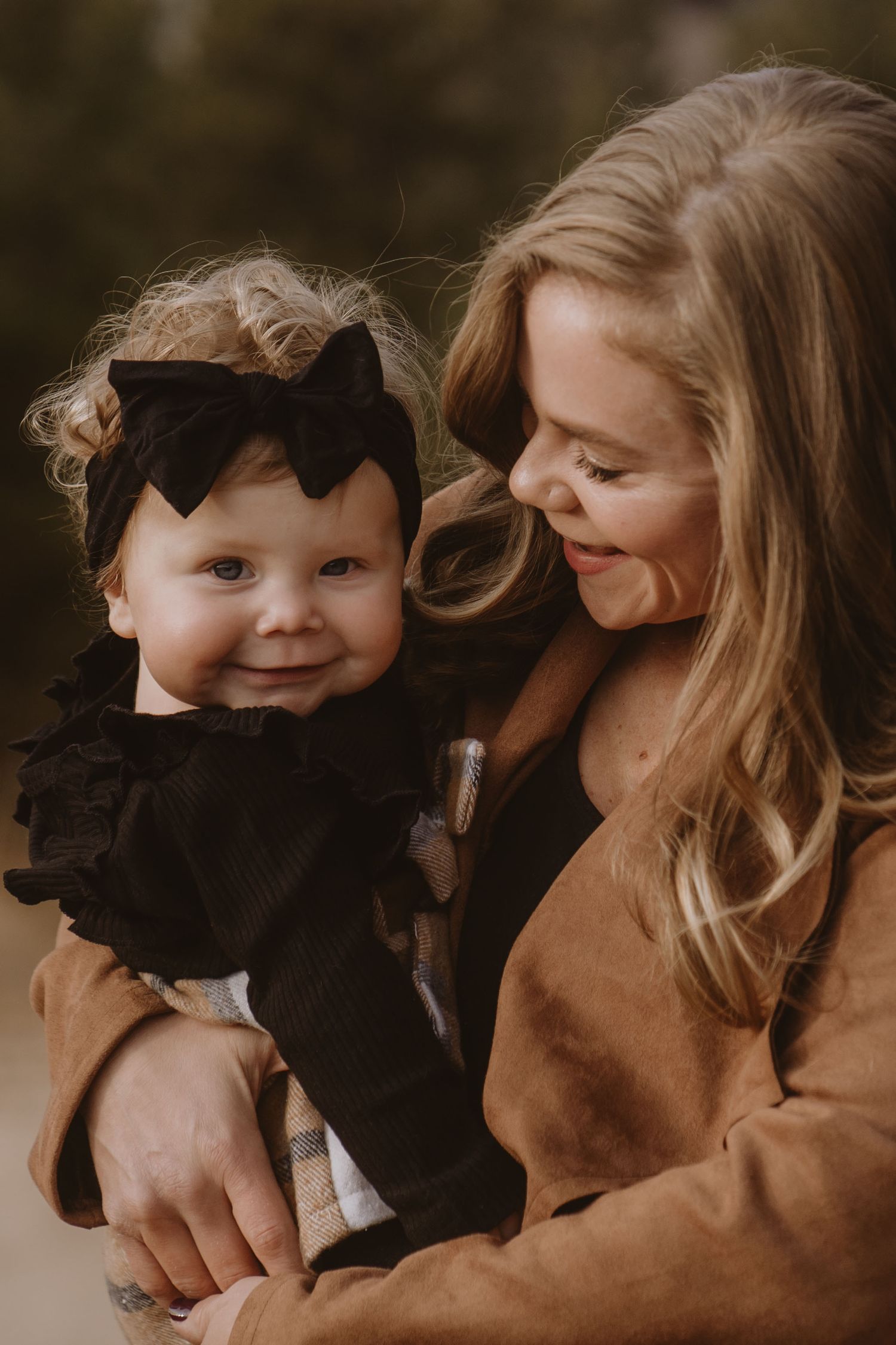 A laughing toddler in a blue shirt peeks through wooden fence rails while a woman holds a baby above.