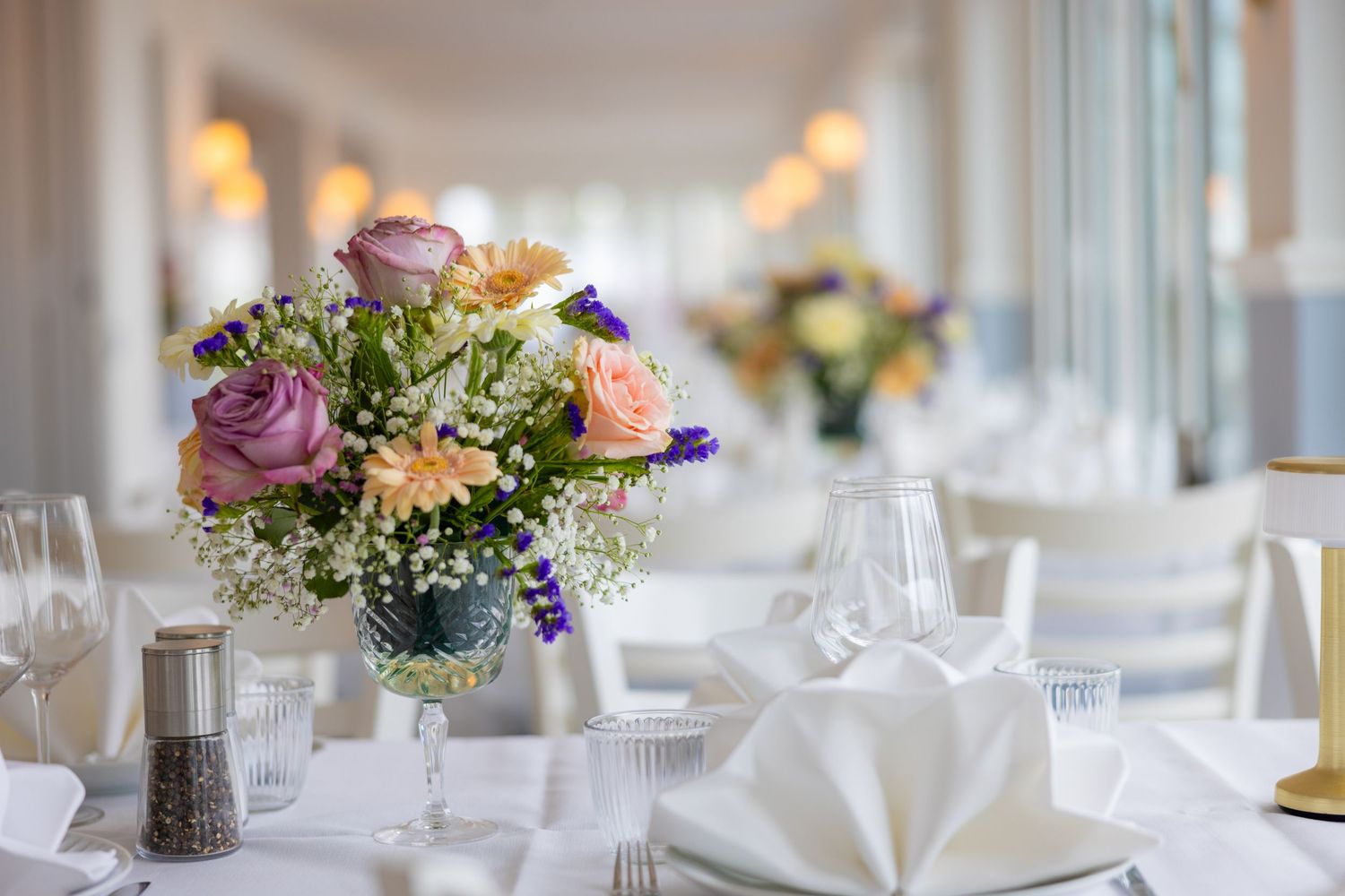 Elegant wedding reception table with floral centerpiece of roses and wildflowers, white linens, napkins, and glassware.