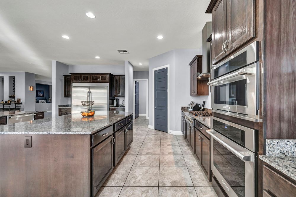 Large kitchen featuring dark cabinetry, granite island, stainless steel double ovens, and tile floors.