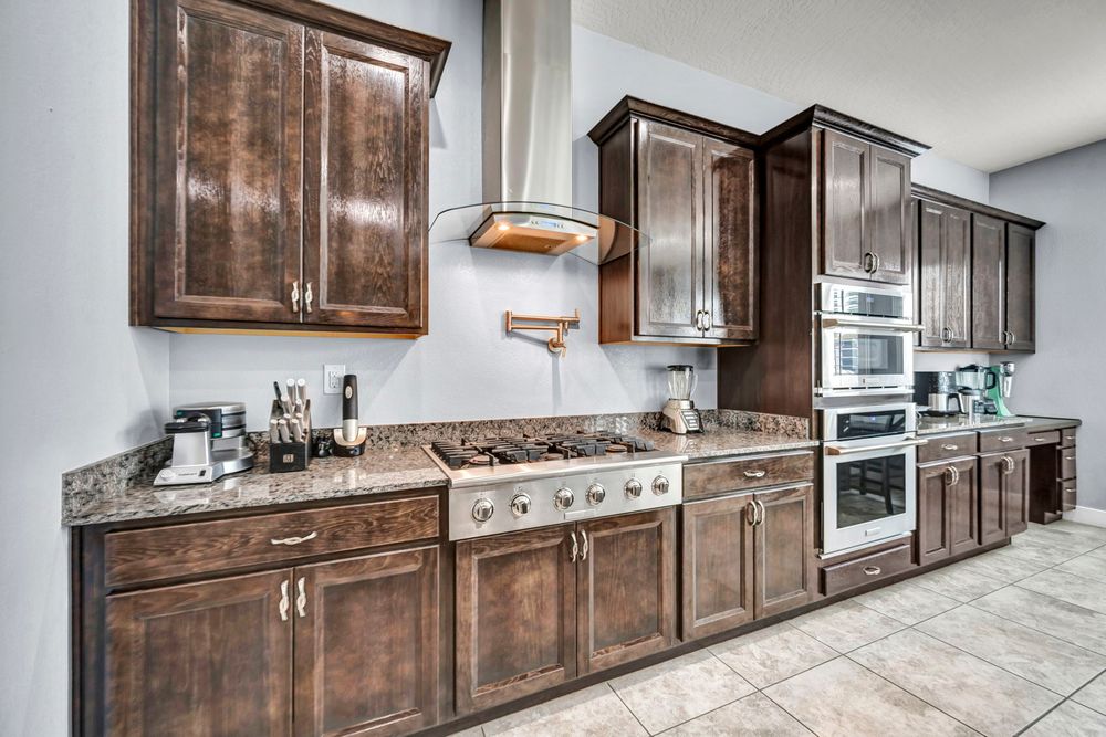 Kitchen wall with dark wood cabinets, granite counters, stainless steel gas cooktop, and range hood.