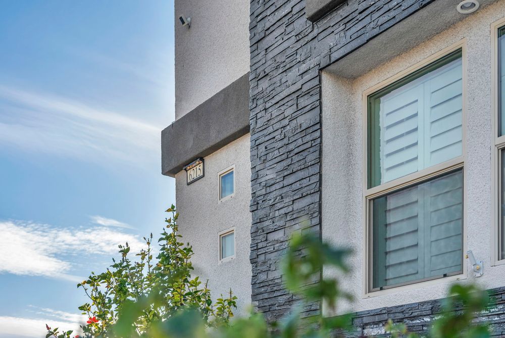 Exterior detail of modern home with stacked stone accent wall, stucco finish, and shuttered windows.