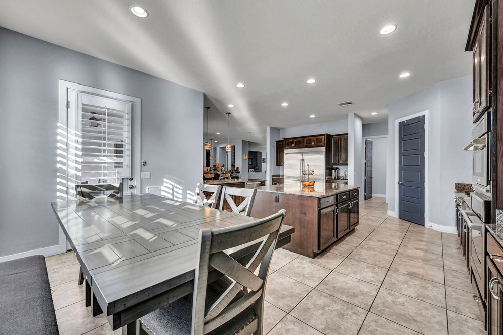 Open-concept dining and kitchen area with gray walls, tile floors, dark cabinetry, and recessed lighting.