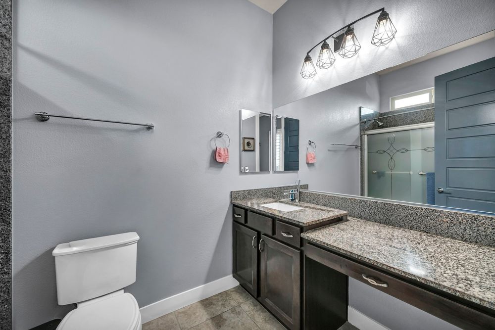 Modern bathroom with dark vanity, granite countertop, large mirror, and glass shower enclosure.