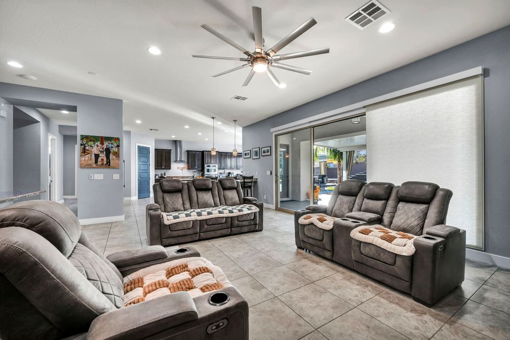 Spacious living room with recliner sofas, ceiling fan, tile floors, and sliding glass doors to patio.