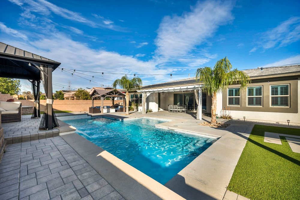 Resort-style backyard with rectangular pool, green lawn, pergola, covered patio, and string lights.