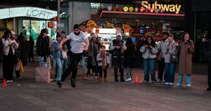 A man dances on a busy Times Square sidewalk near a Subway restaurant as onlookers watch at night.