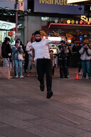 Street performer dancing in Times Square NYC at night, crowd watching, wearing white shirt and black pants.