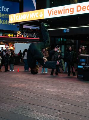A breakdancer performs a backflip in Times Square NYC at night with crowds watching near a Candy NYC store.