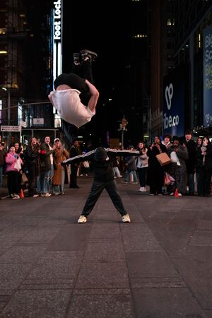 Street performers execute an acrobatic lift in Times Square NYC at night with a crowd of spectators watching.