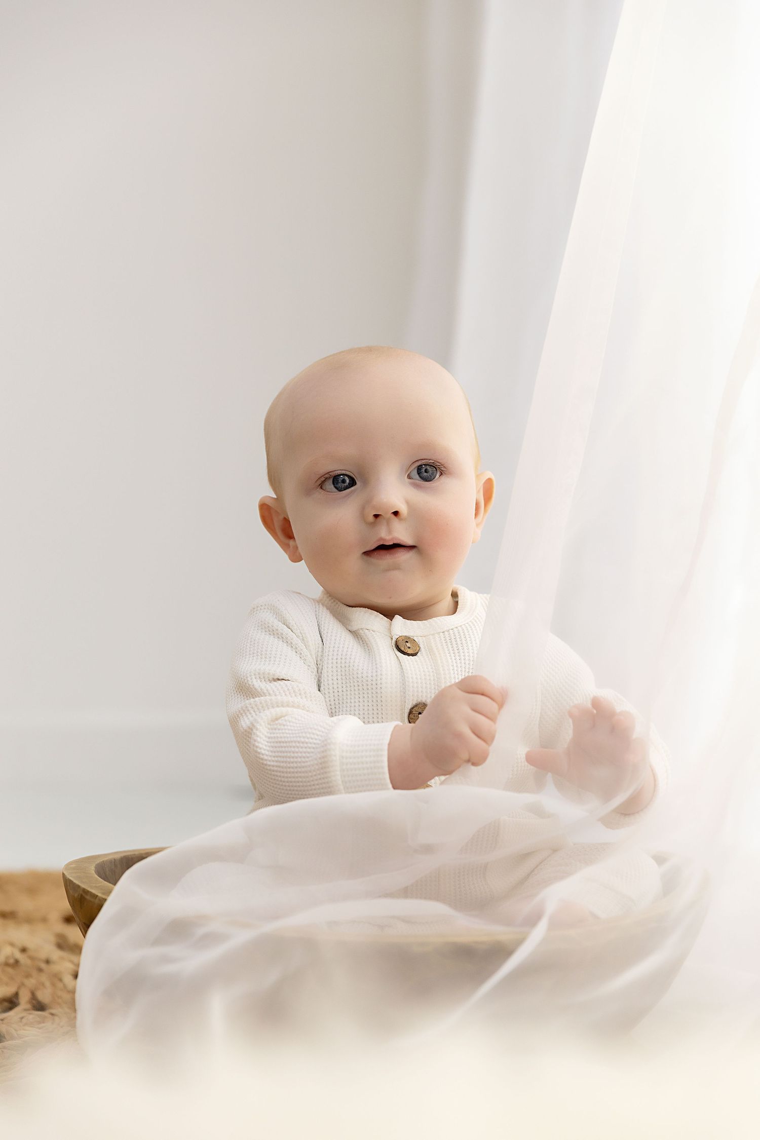 Little boy sitting in a bowl playing with curtains at his sitter session in Coventry with Shelly Loxton Photography
