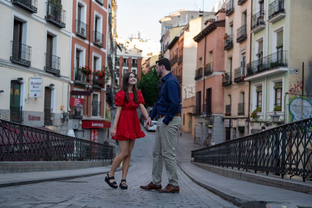 Couple in red dress and blue shirt holding hands on cobblestone street in Madrid, Spain.