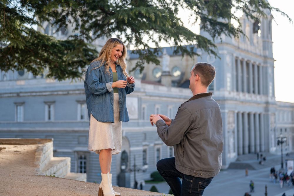 Man proposes on one knee to woman outdoors near historic European building, romantic marriage proposal moment.